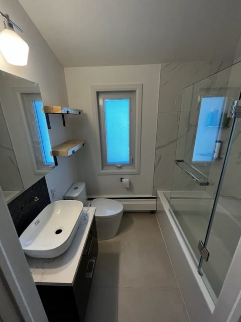 Maison r&eacute;nov&eacute;e avec rev&ecirc;tement blanc, toit noir et briques, entour&eacute;e de v&eacute;g&eacute;tation.