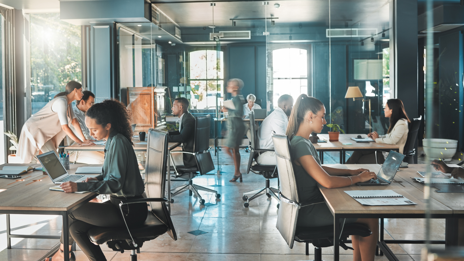 Open office with people working on laptops, interacting. Bright, modern space.