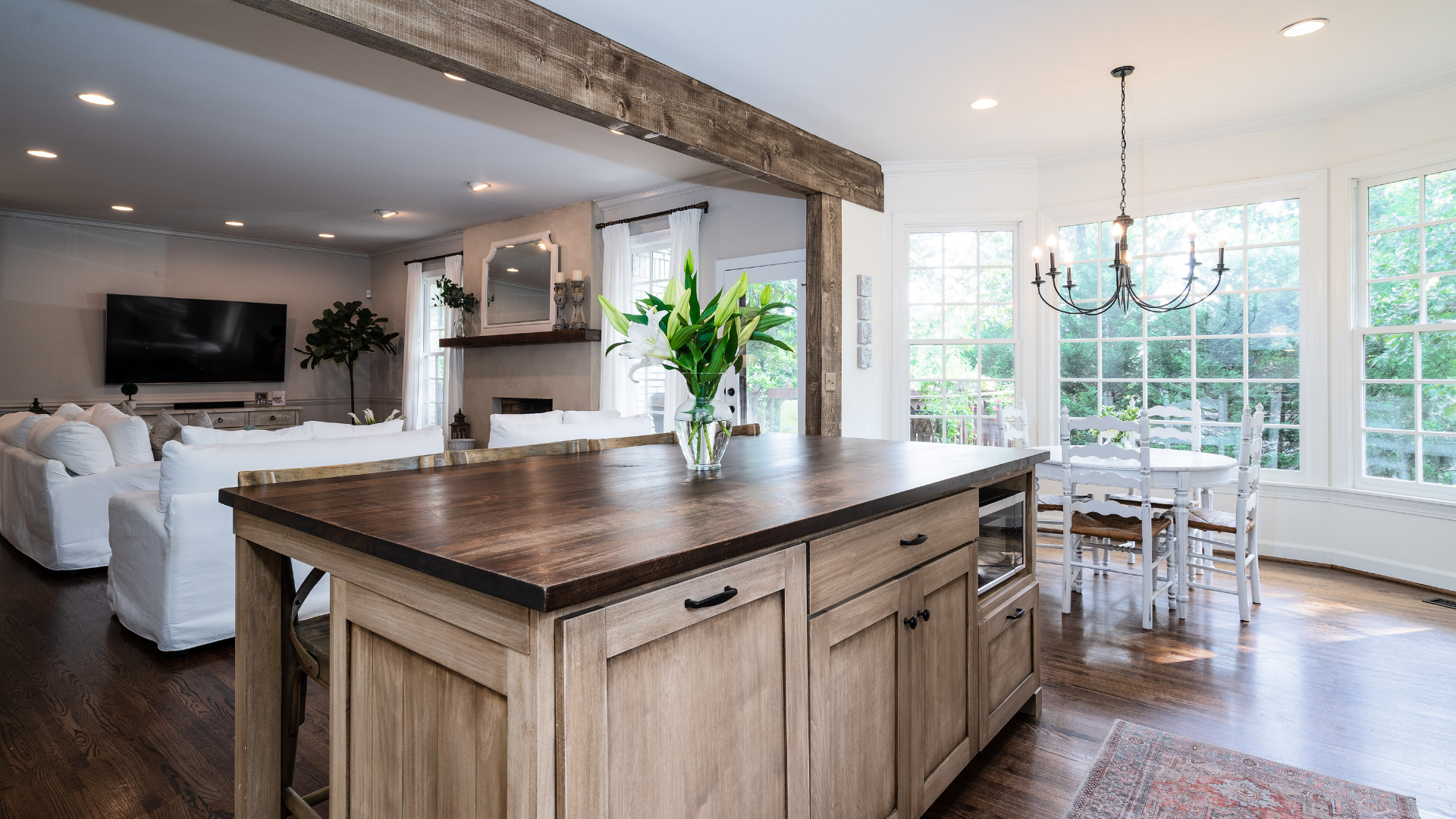 Open kitchen with wooden island, living room, and dining area with abundant natural light.