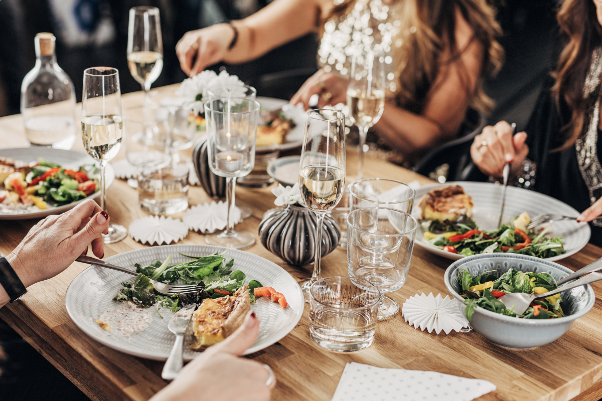 A group of people are sitting at a table eating food and drinking wine.