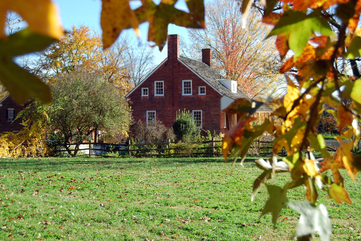 A red brick house is behind a fence in a field
