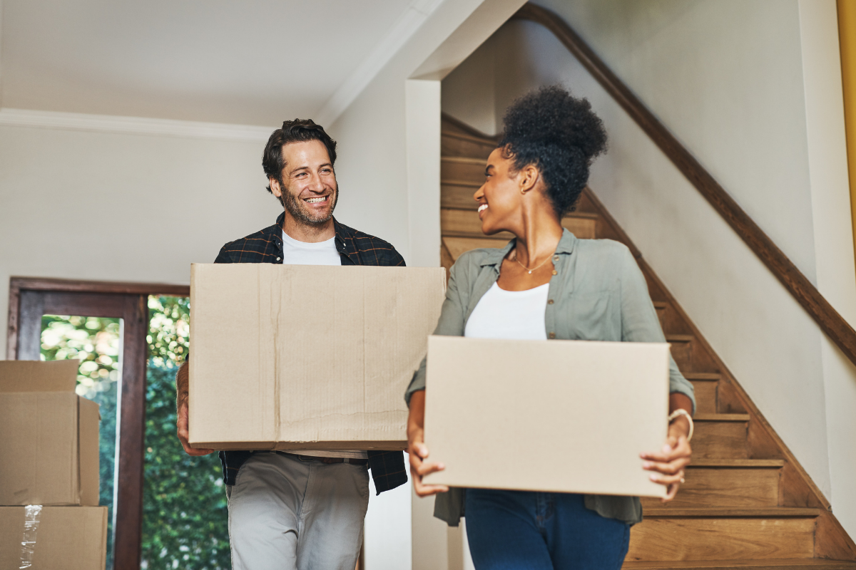 A man and a woman are carrying cardboard boxes into their new home