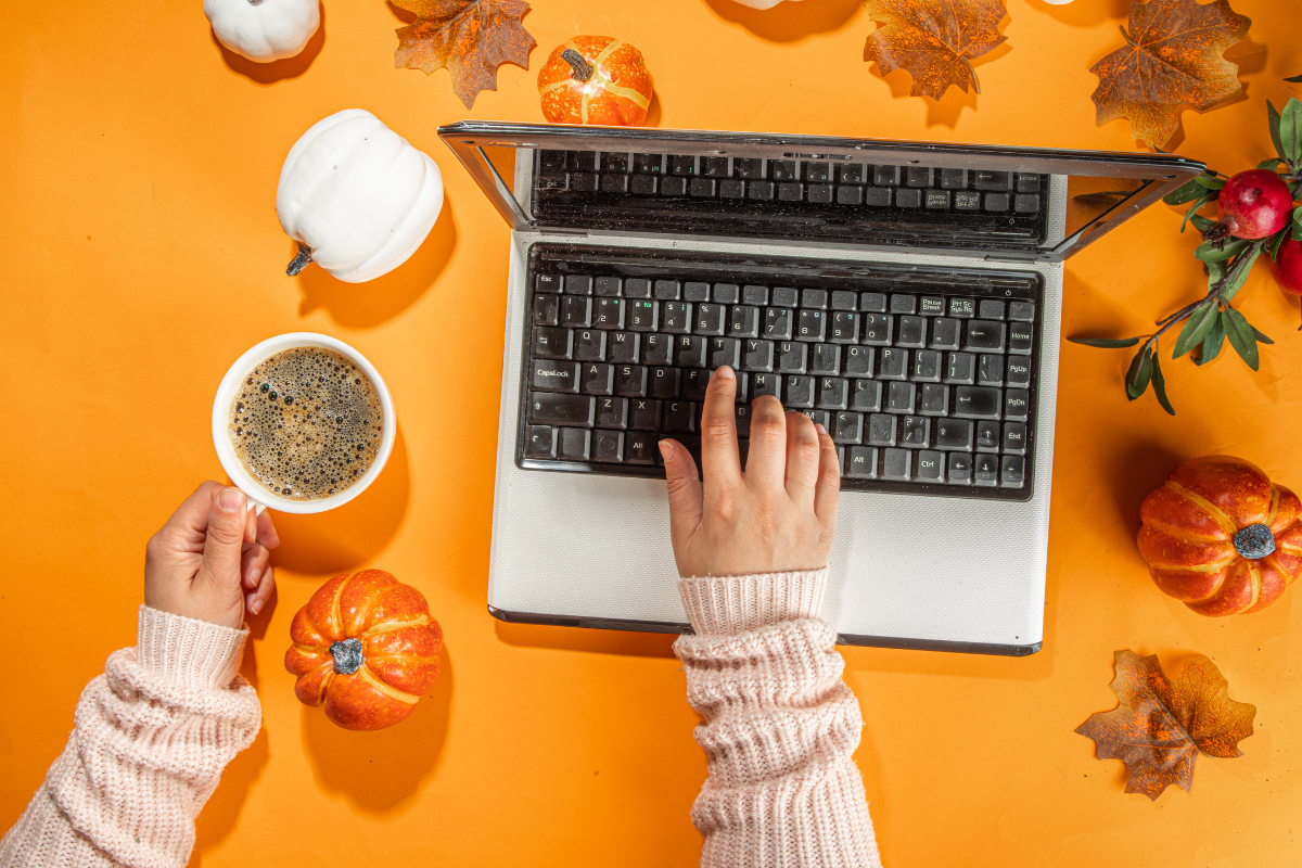 A person is typing on a laptop while holding a cup of coffee