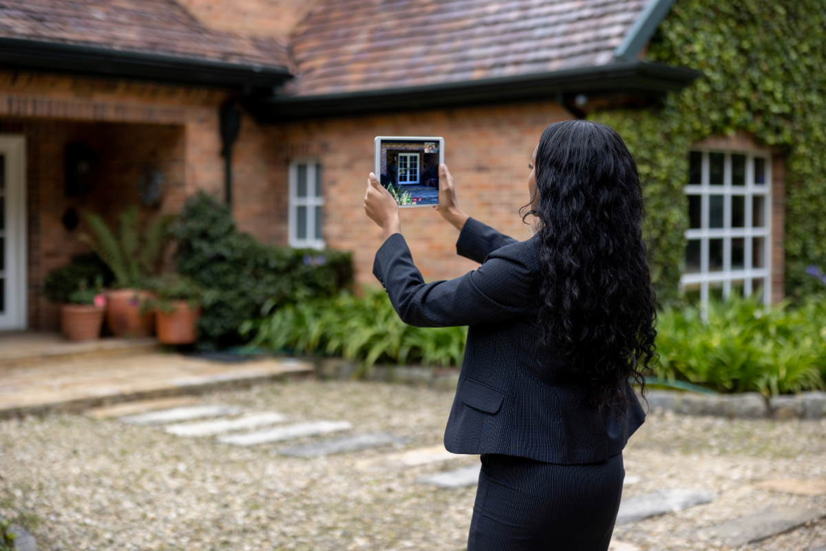 A woman is holding a tablet in front of a house.