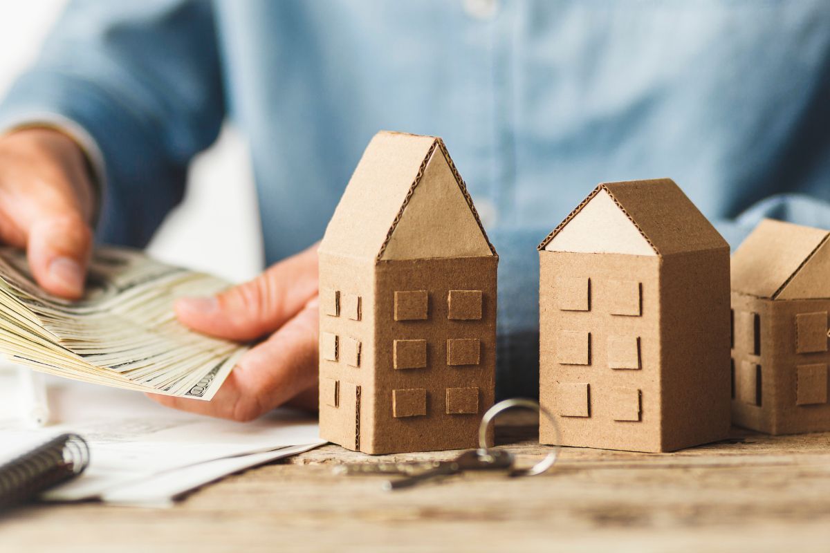 A person is holding a bunch of money next to cardboard houses