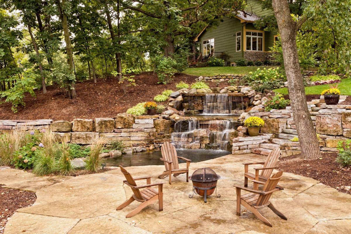 A patio with chairs and a fire pit in front of a waterfall