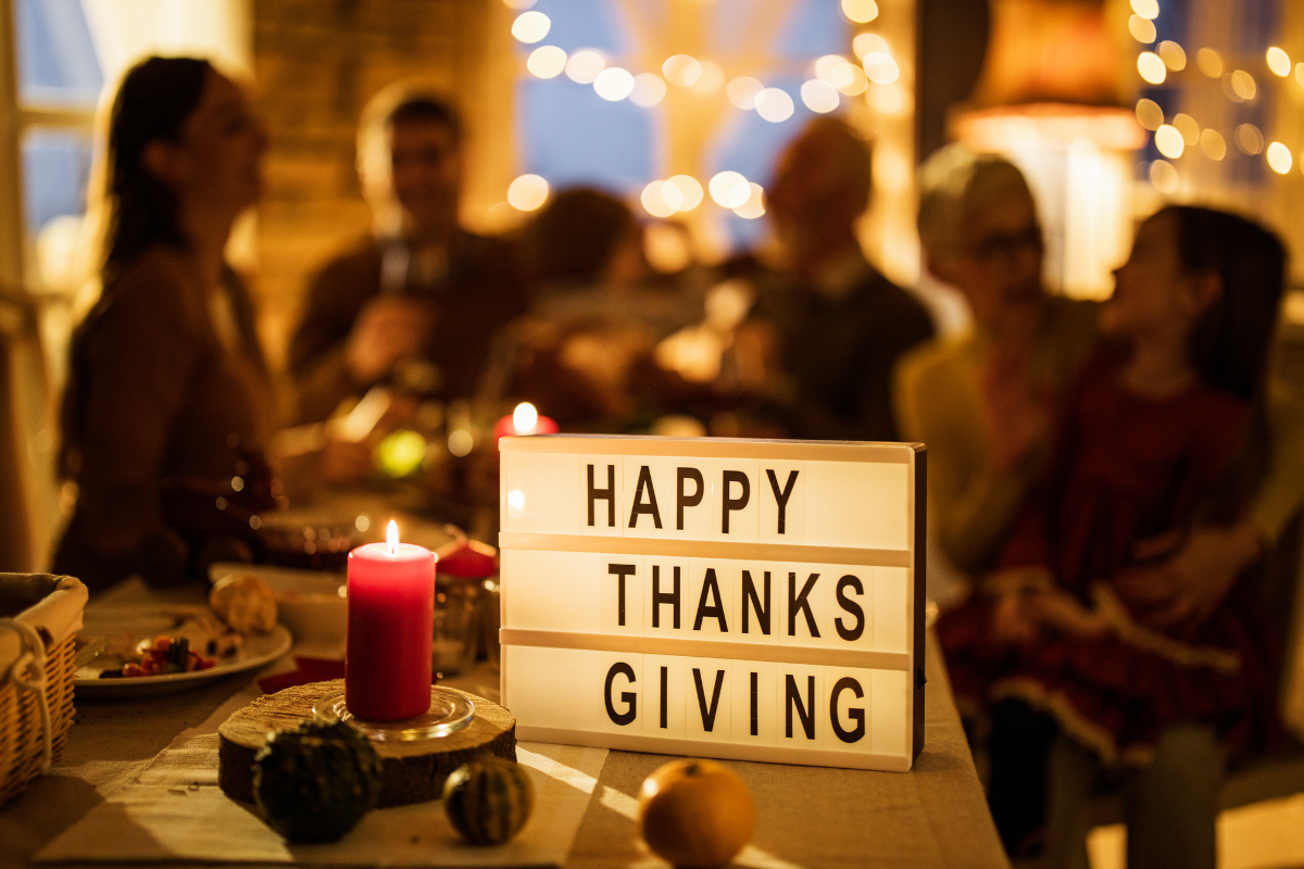 A group of people are sitting around a table with a sign that says happy thanksgiving