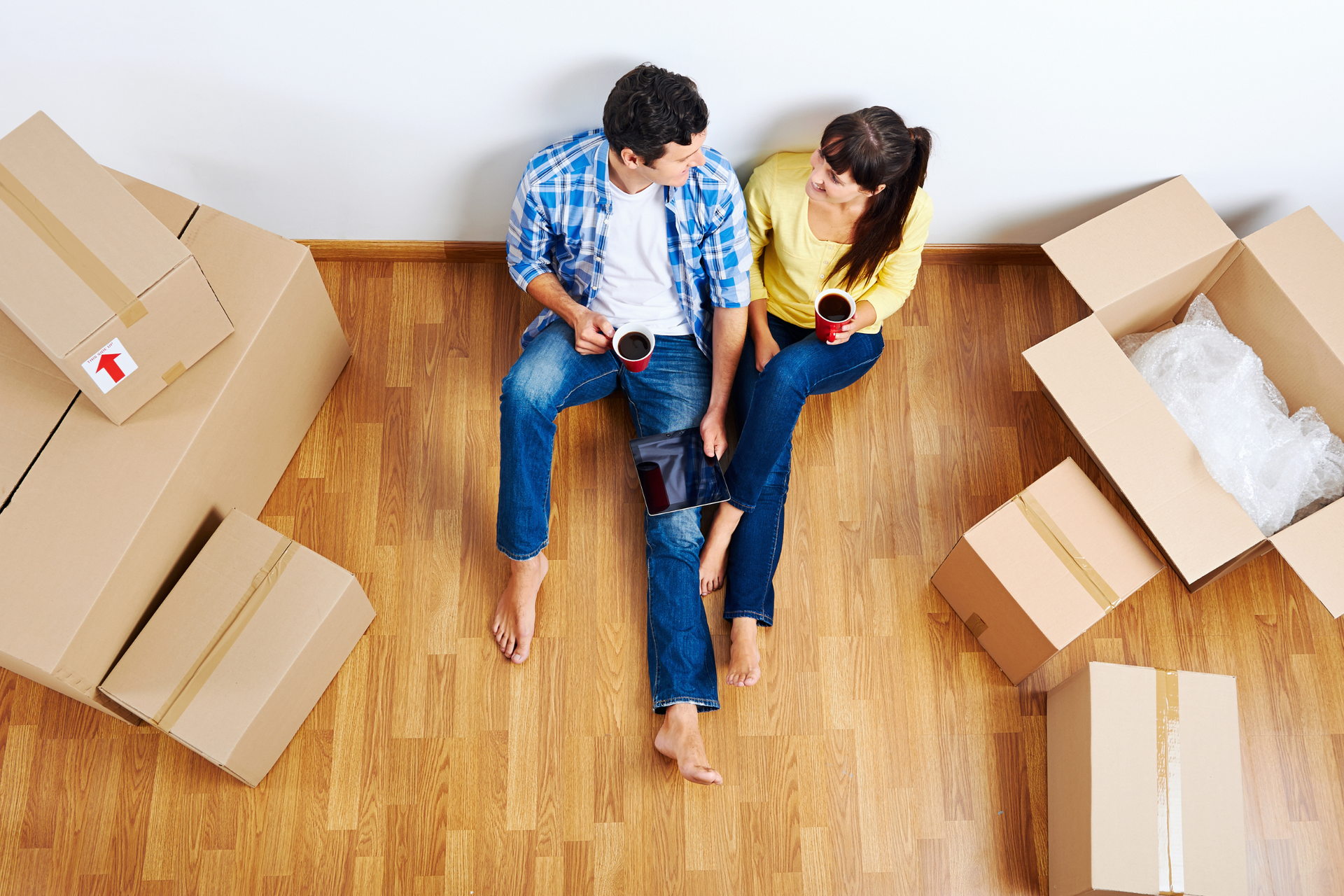 Couple sitting on the floor sharing coffee with moving boxes