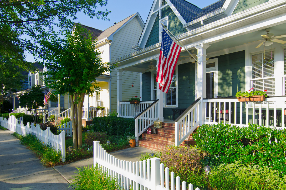 A green house with a white picket fence and an american flag on the porch