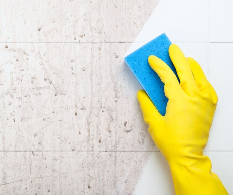 A person wearing yellow gloves is cleaning a wall with a blue sponge.