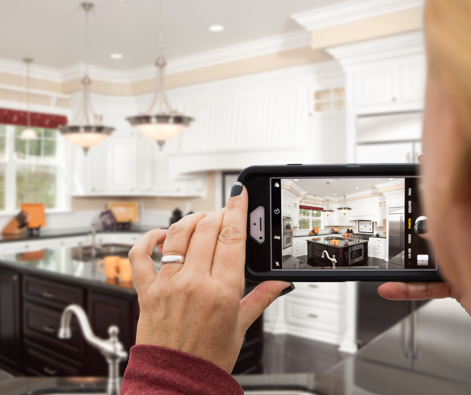 A woman is taking a picture of a kitchen with her phone