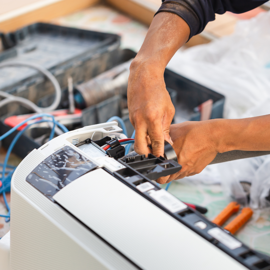 A man is fixing an air conditioner with a pair of pliers