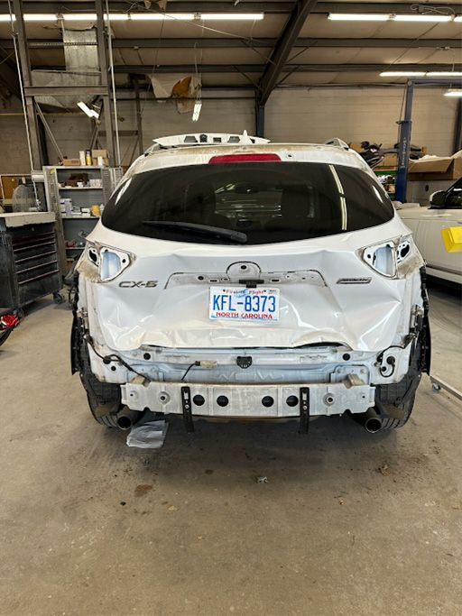 A white car is sitting in a garage with its rear end missing.