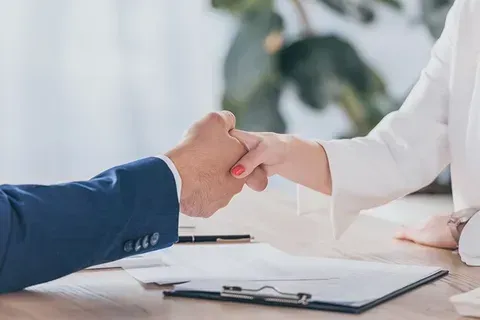 A man and a woman are shaking hands over a table.