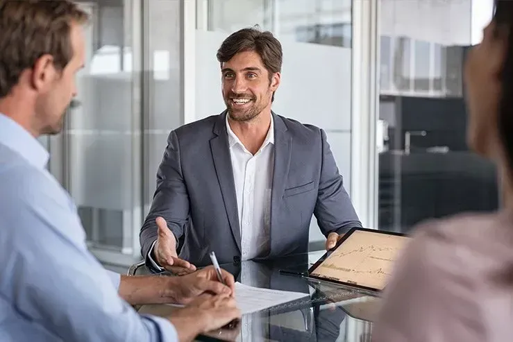 A man in a suit is sitting at a table talking to two people.