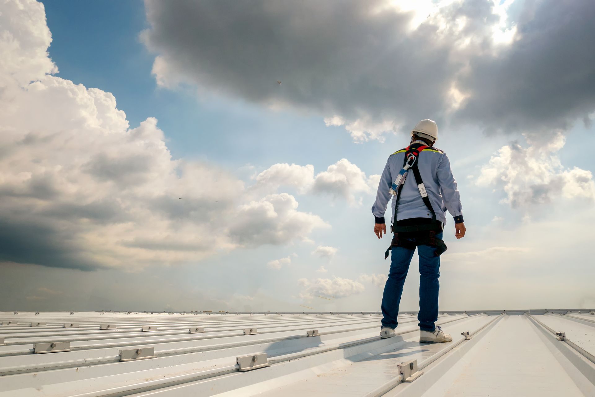 Man on a rooftop, wearing safety harness, looking out at cloudy sky