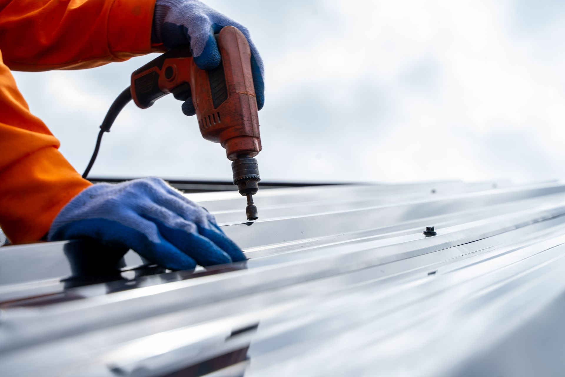 Person in orange work attire using a drill to install a metal roof