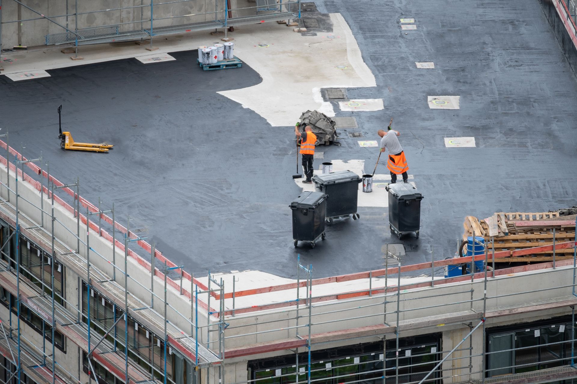 Construction workers on a roof, near trash cans and a forklift