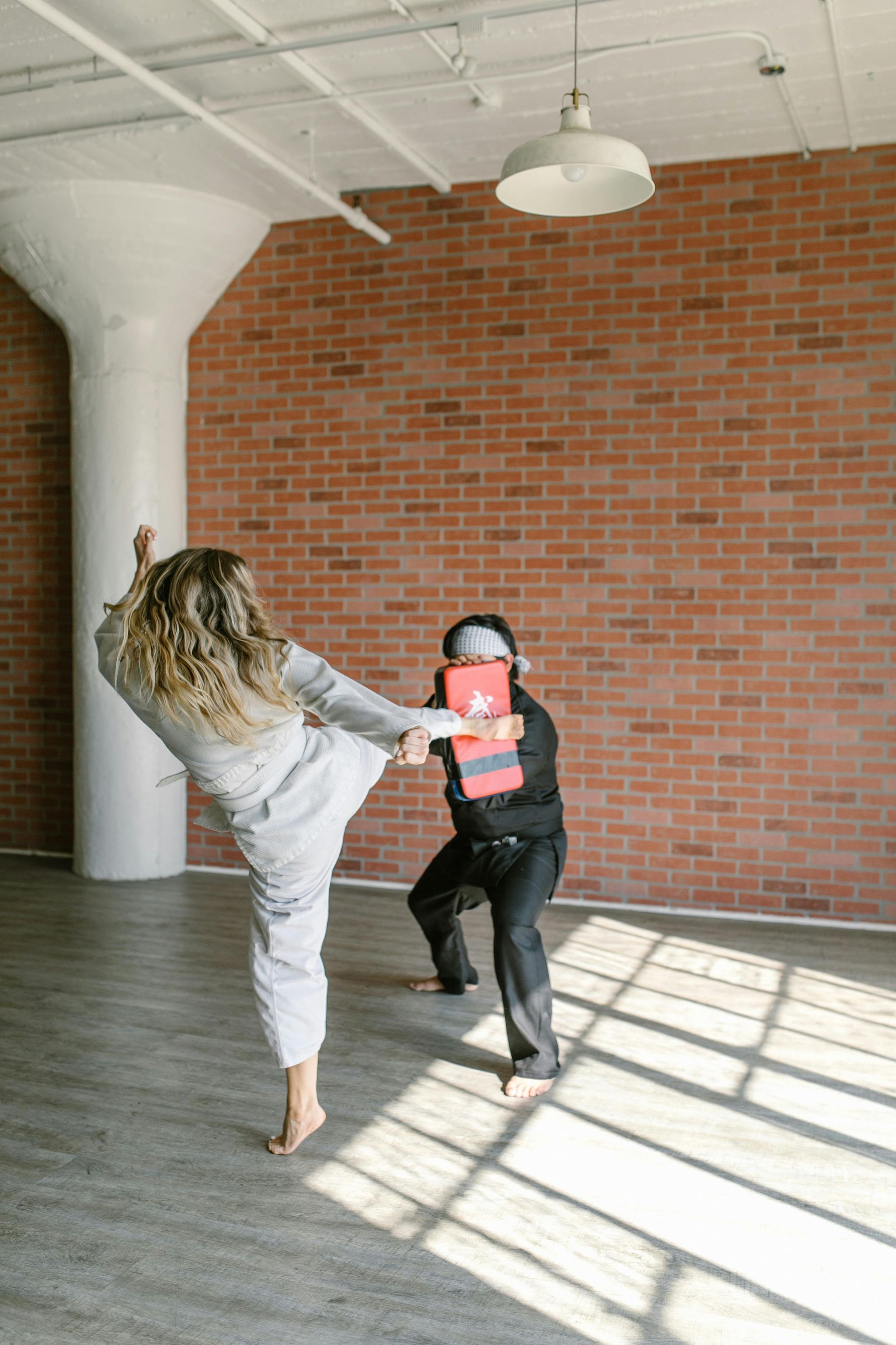 Woman kicking a target held by a person in a practice space.