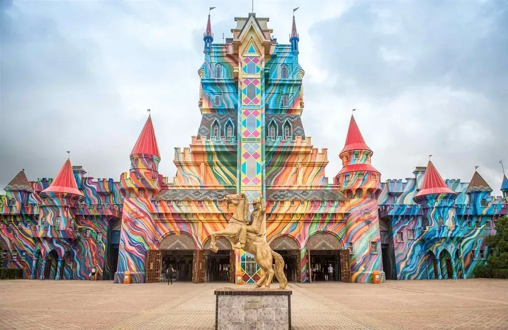 Um castelo de cores brilhantes com redemoinhos de arco-íris, torres com topos vermelhos e uma estátua de ouro na frente.