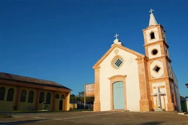 Igreja com fachada branca, detalhes em laranja e um alto campanário contra um céu azul.