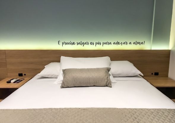 Uma cama com lençóis e travesseiros brancos em um quarto de hotel com uma citação na parede.