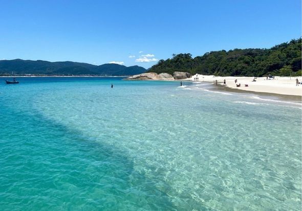 Uma praia com um barco na água e montanhas ao fundo