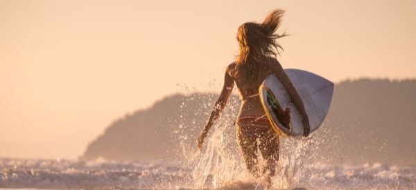 Uma mulher está saindo do oceano com uma prancha de surf.