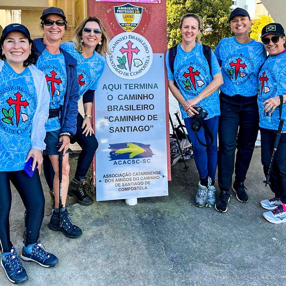 A group of people standing in front of a sign that says aqui termina o caminho brasileiro caminho de santiago