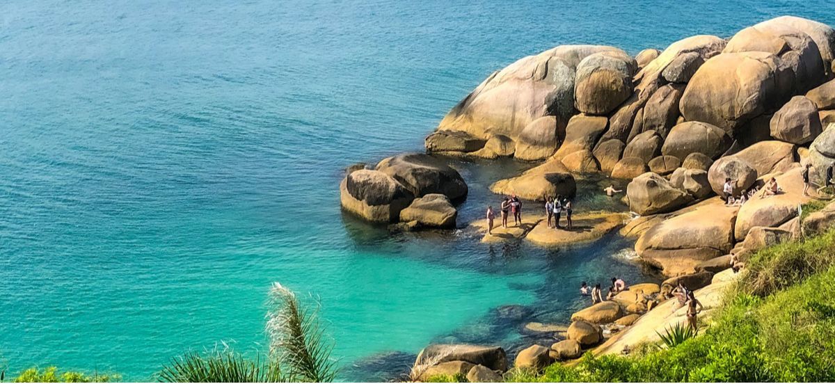 Um grupo de pessoas está em uma costa rochosa próximo a um corpo de água.