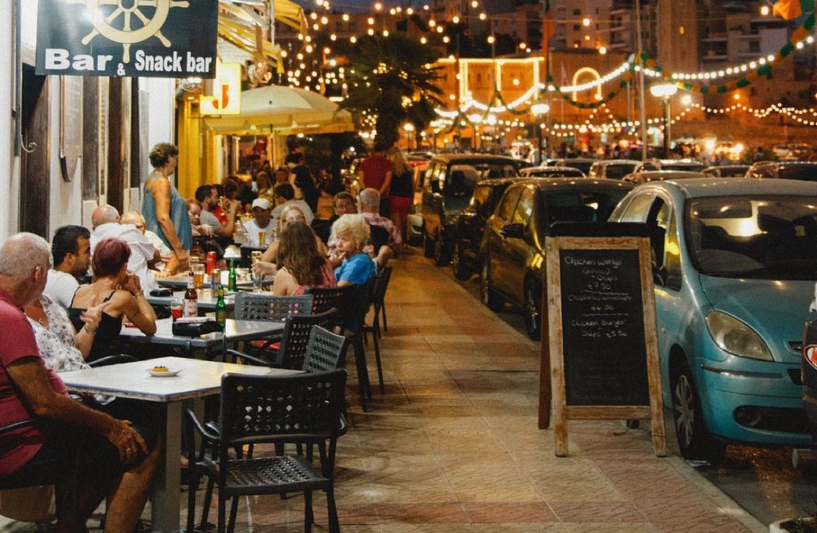 Um grupo de pessoas está sentado em mesas do lado de fora de um bar/lanchonete