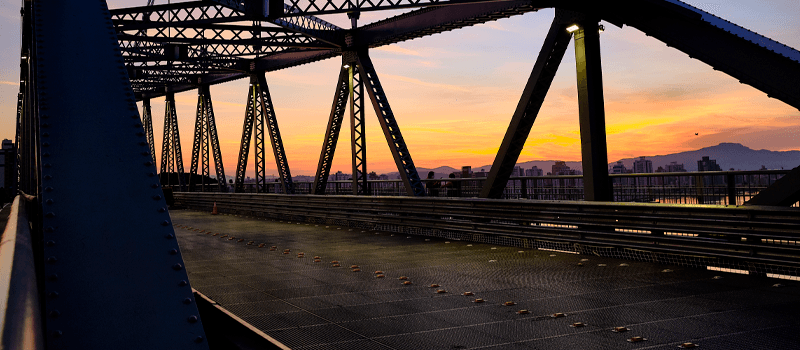 Uma ponte sobre um corpo de água com um pôr do sol ao fundo.