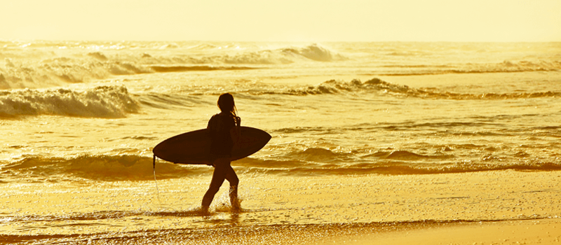 Um surfista está caminhando na praia carregando uma prancha de surf.