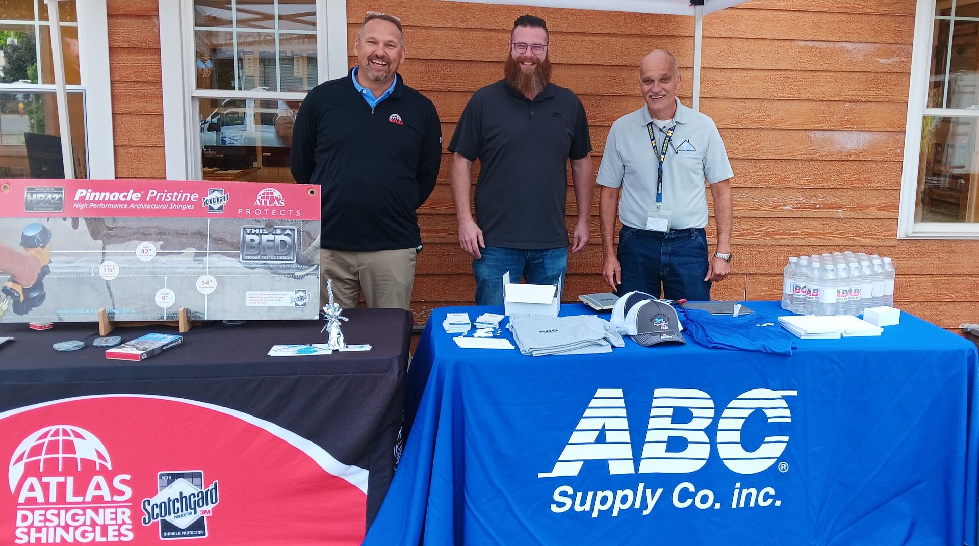 Three men standing in front of a table that says abc supply co. inc.