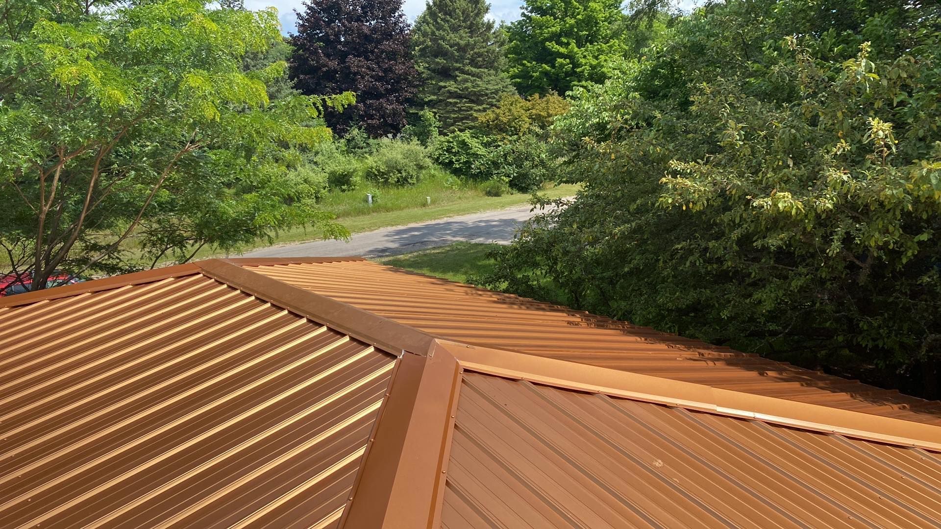 A brown metal roof with trees in the background and a road in the background.