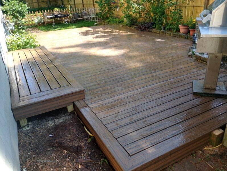 A wooden deck with a grill on it in a backyard.