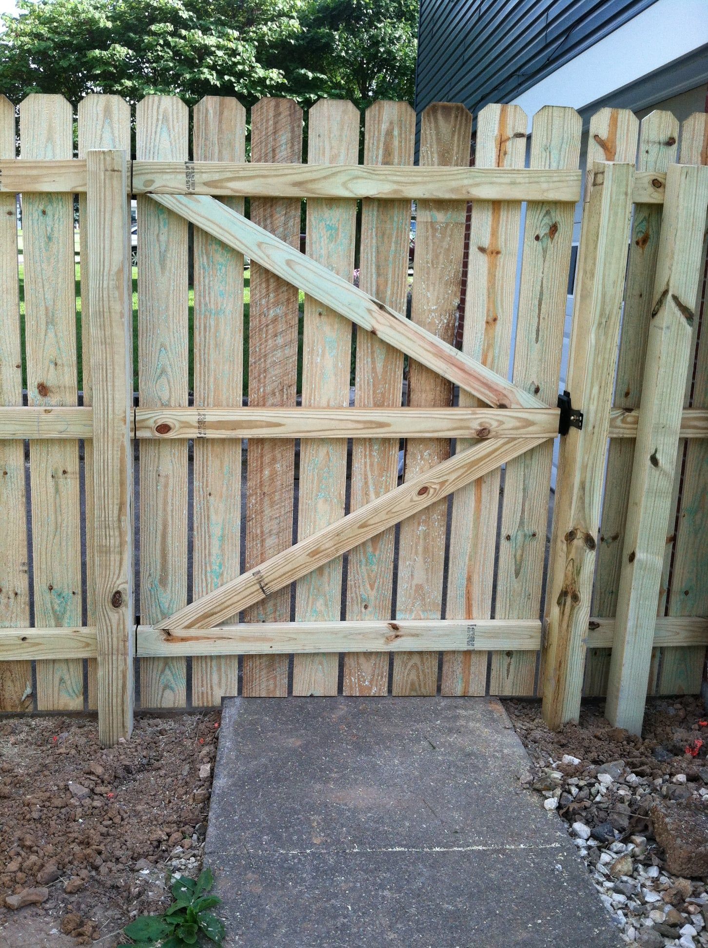 Wooden garden gate with diagonal braces in a fenced backyard, viewed from a concrete path