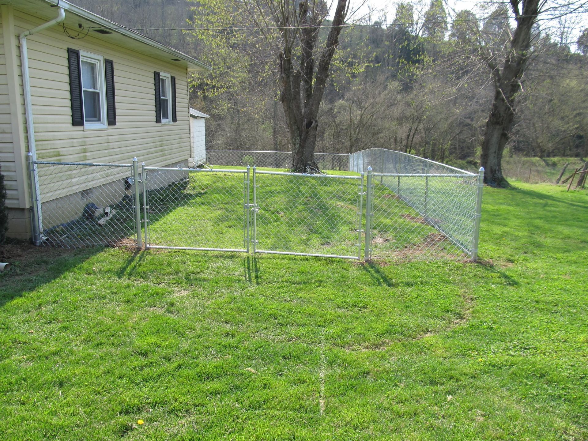 Backyard with a small wire fence enclosure beside a yellow house and grassy yard