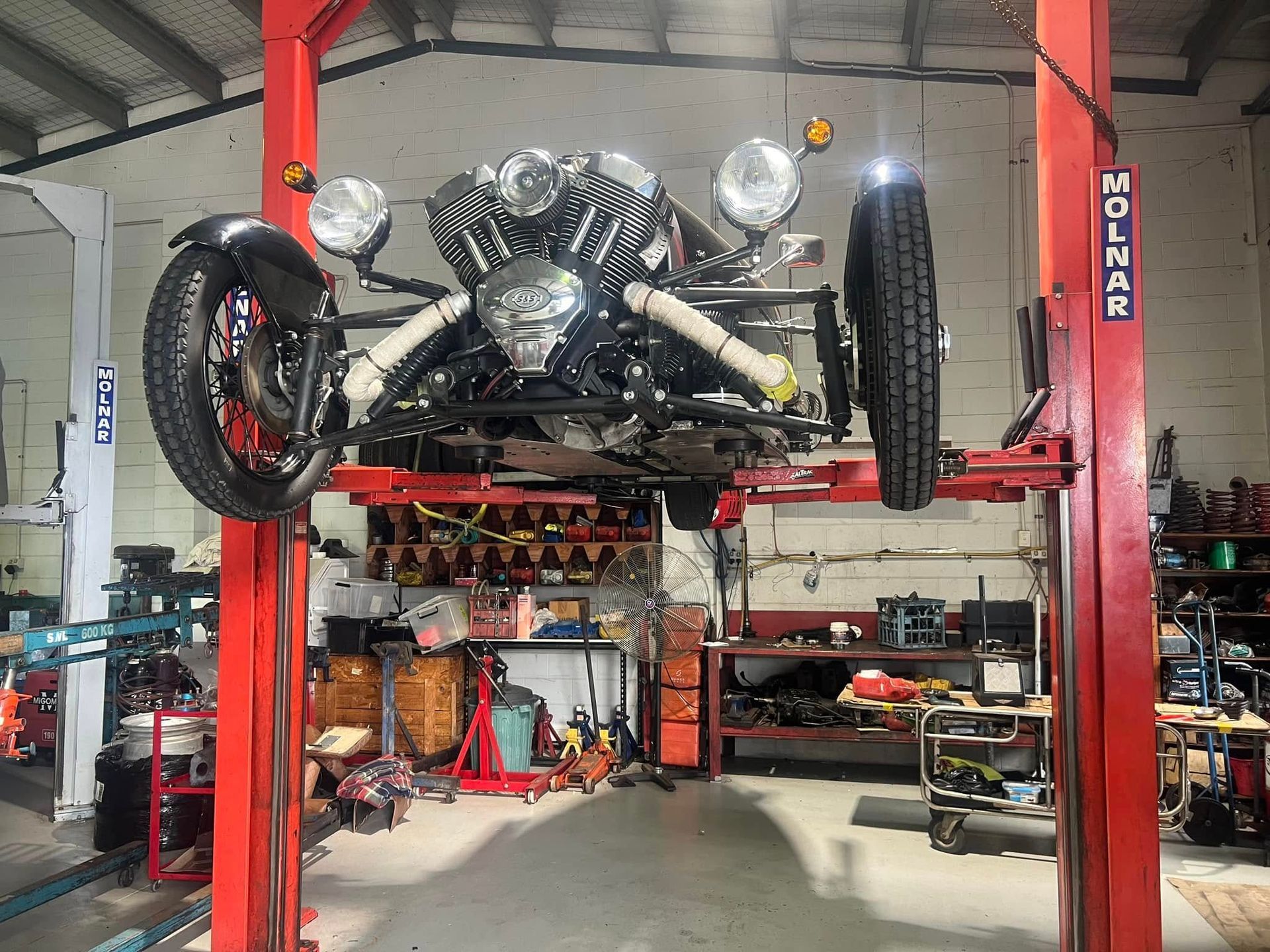 A Three-wheeled Vehicle Is Hoisted On A Red Hydraulic Lift — Auto Inspections & Road Services N.T in Woolner, NT