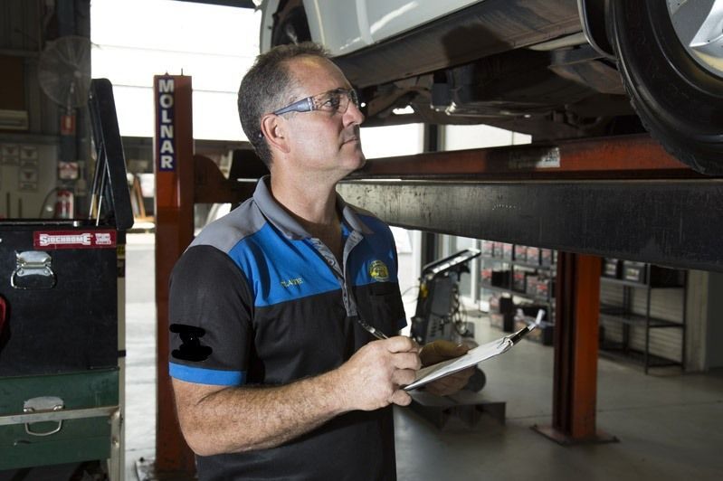 Mechanic in Blue Work Shirt Inspecting a Vehicle on a Lift — Auto Inspections & Road Services N.T in Woolner, NT