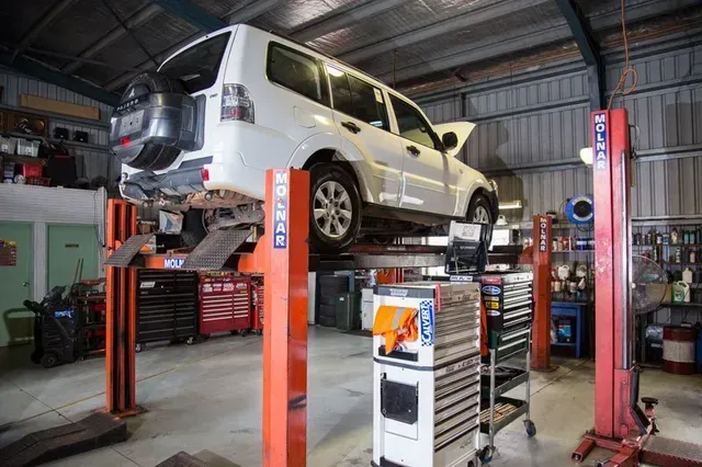 White SUV Lifted on a Red Car Hoist Inside an Auto Repair Garage — Auto Inspections & Road Services N.T in Woolner, NT