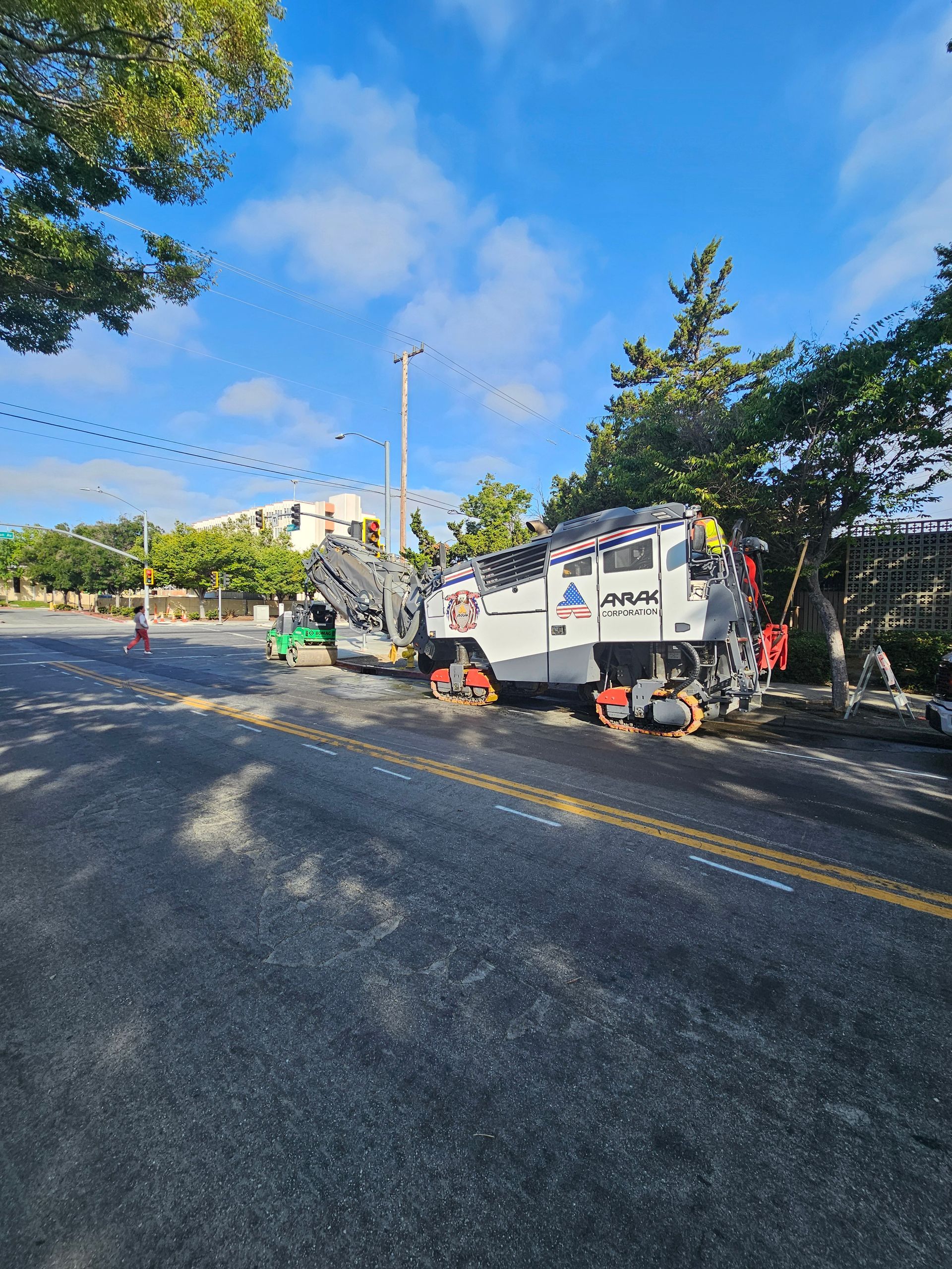 A white specialized construction or rail-maintenance vehicle has veered off a paved road into trees and brush.