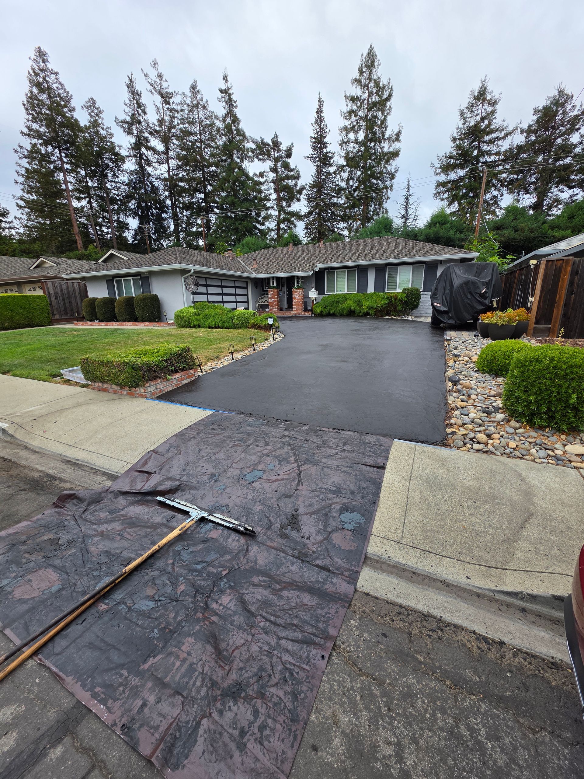 A freshly sealcoated residential driveway with a squeegee lying on a black mat in the foreground.