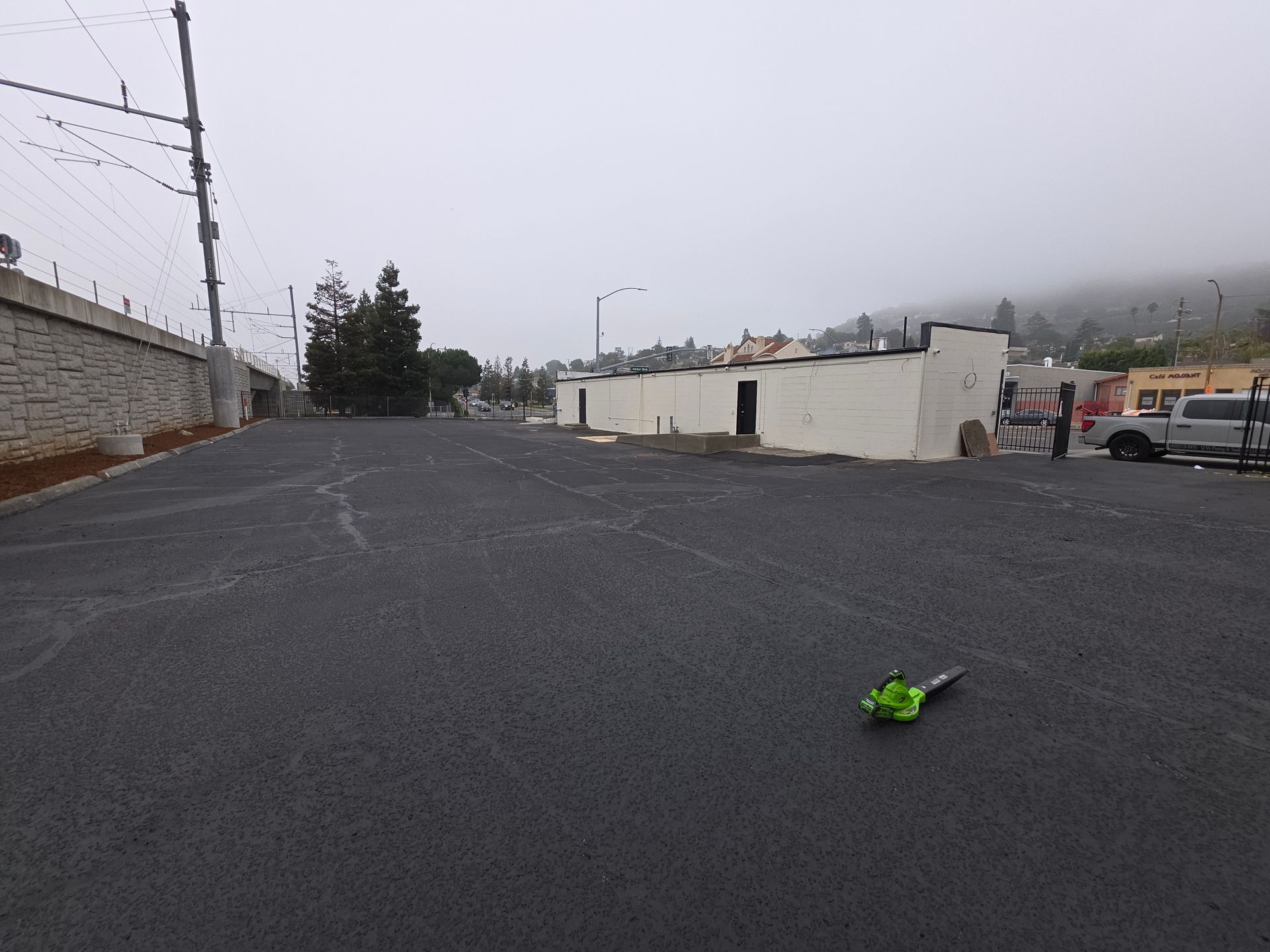 A freshly paved asphalt parking lot on a foggy day, with a small green tool sitting on the ground in the foreground.