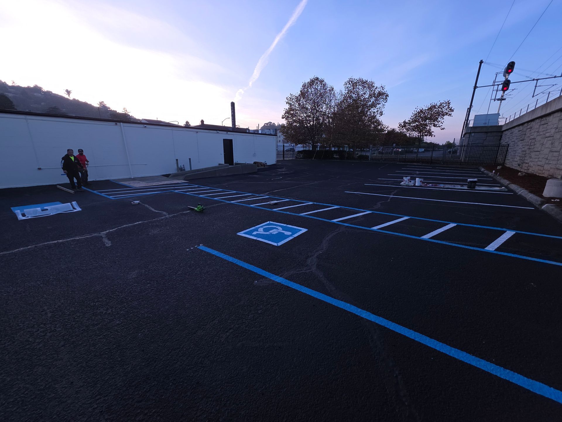 A freshly paved parking lot features bright blue handicapped parking symbols and painted lines, with two people nearby.