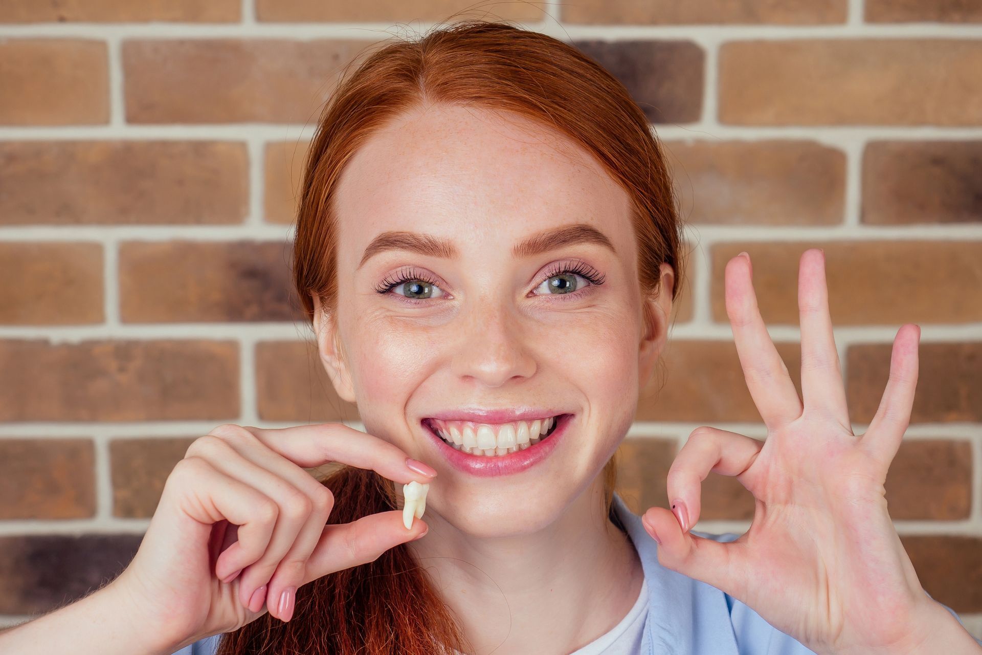 Woman with red hair smiling, holding a tooth, and making an 