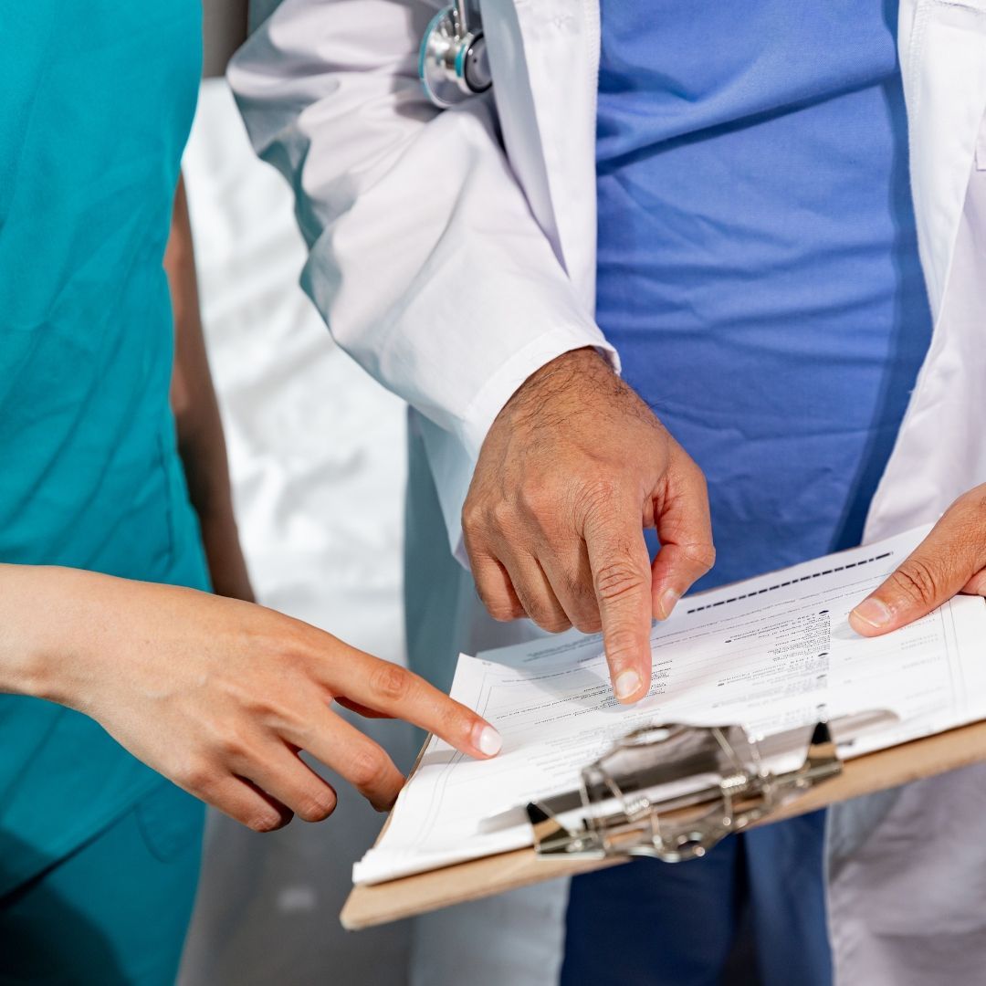 Doctor and nurse reviewing a medical chart; doctor's hand points to a line while the nurse's hand points as well.