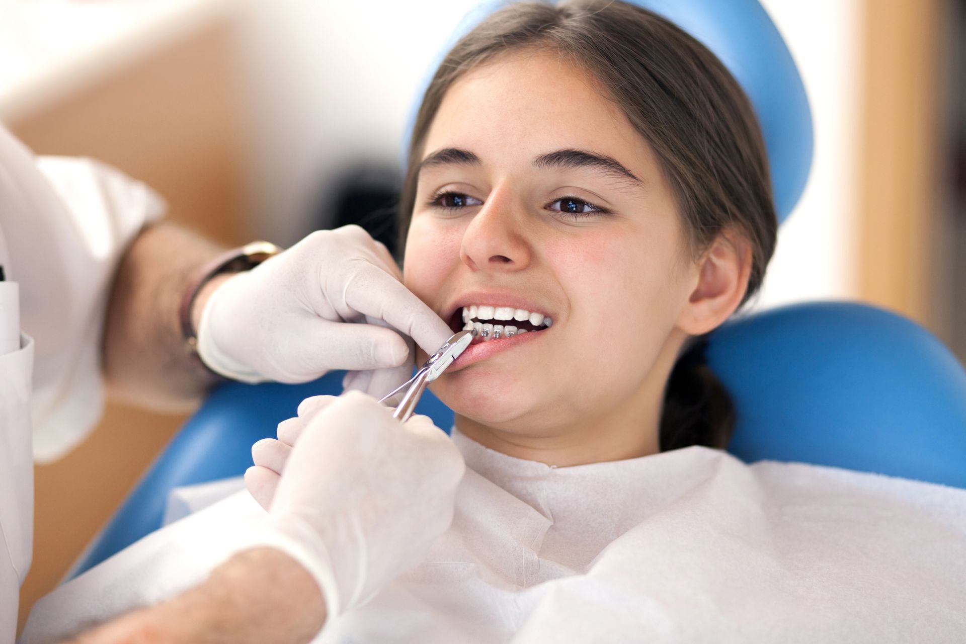 A dentist examines a young woman's teeth. She sits in a dental chair, wearing a bib, while the dentist holds an instrument in her mouth.