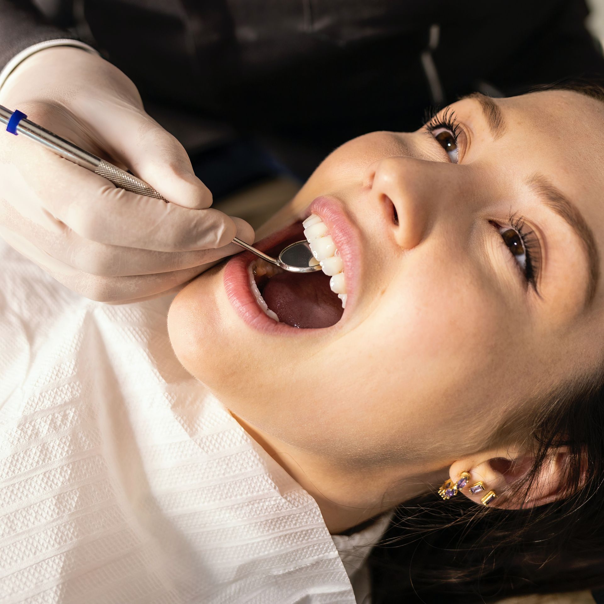 Woman at the dentist, mouth open while the dentist examines her teeth with a mirror.