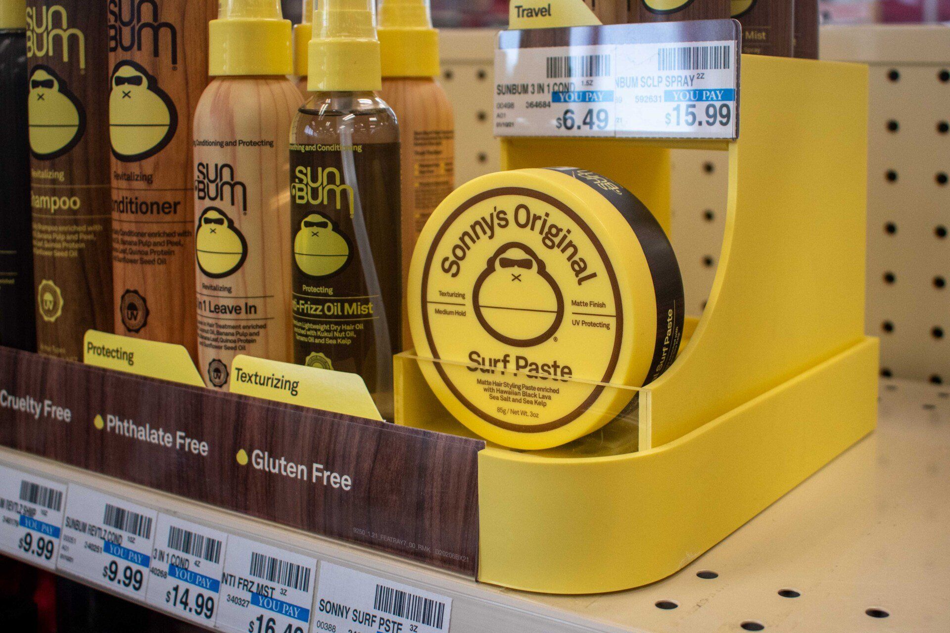 Yellow Sun Bum hair pastes and squeeze bottles are displayed on a grocery store shelf.